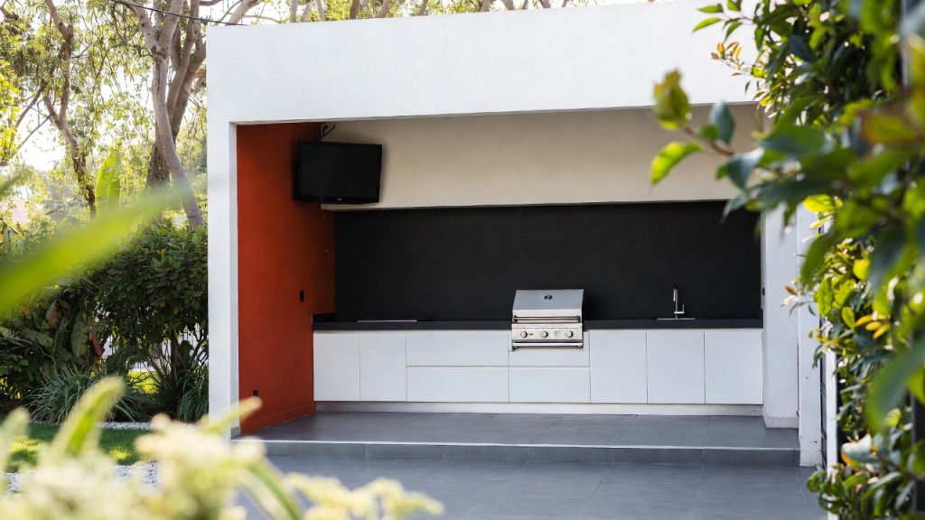 Outdoor kitchen with red wall, barbecue and TV — ConstanKitchen client project